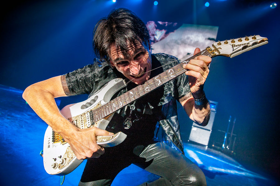 Steve Vai playing a white guitar under blue and gold light, State Theatre, New Brunswick